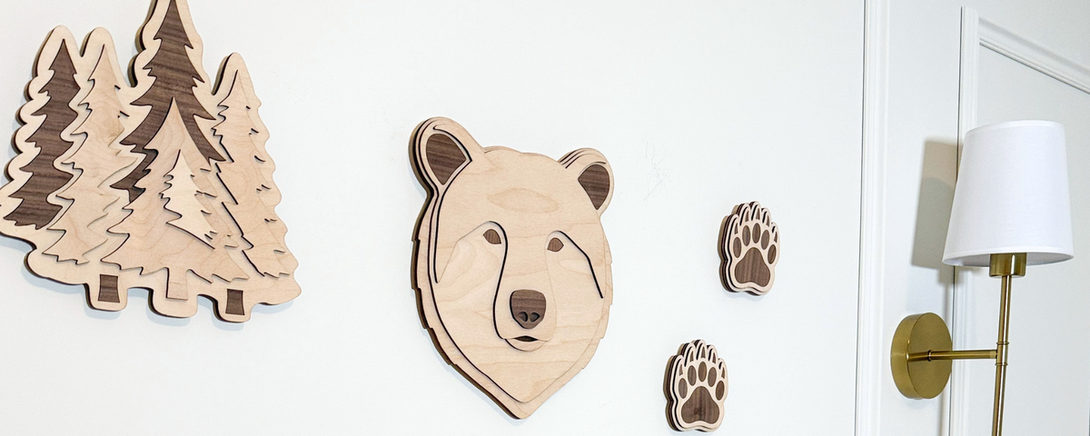 Wooden bear, evergreen trees, and bear paw prints and framed illustrations of woodland creatures in gold frames on a light background
