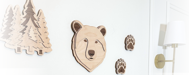 Wooden bear, evergreen trees, and bear paw prints and framed illustrations of woodland creatures in gold frames on a light background