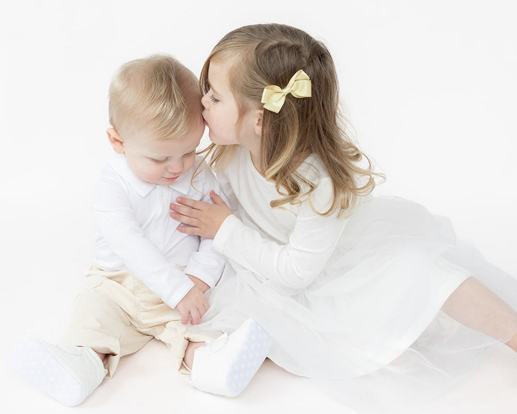 baby boy and baby girl in white outfits sitting close together on a minimalist white background