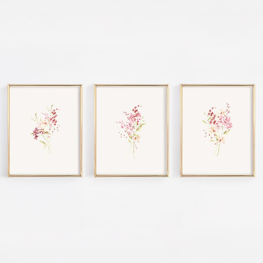 A set of three vertical gold-framed nursery wall art prints featuring different botanical bundles of dusty rose and burgundy wildflowers on a crisp white background.