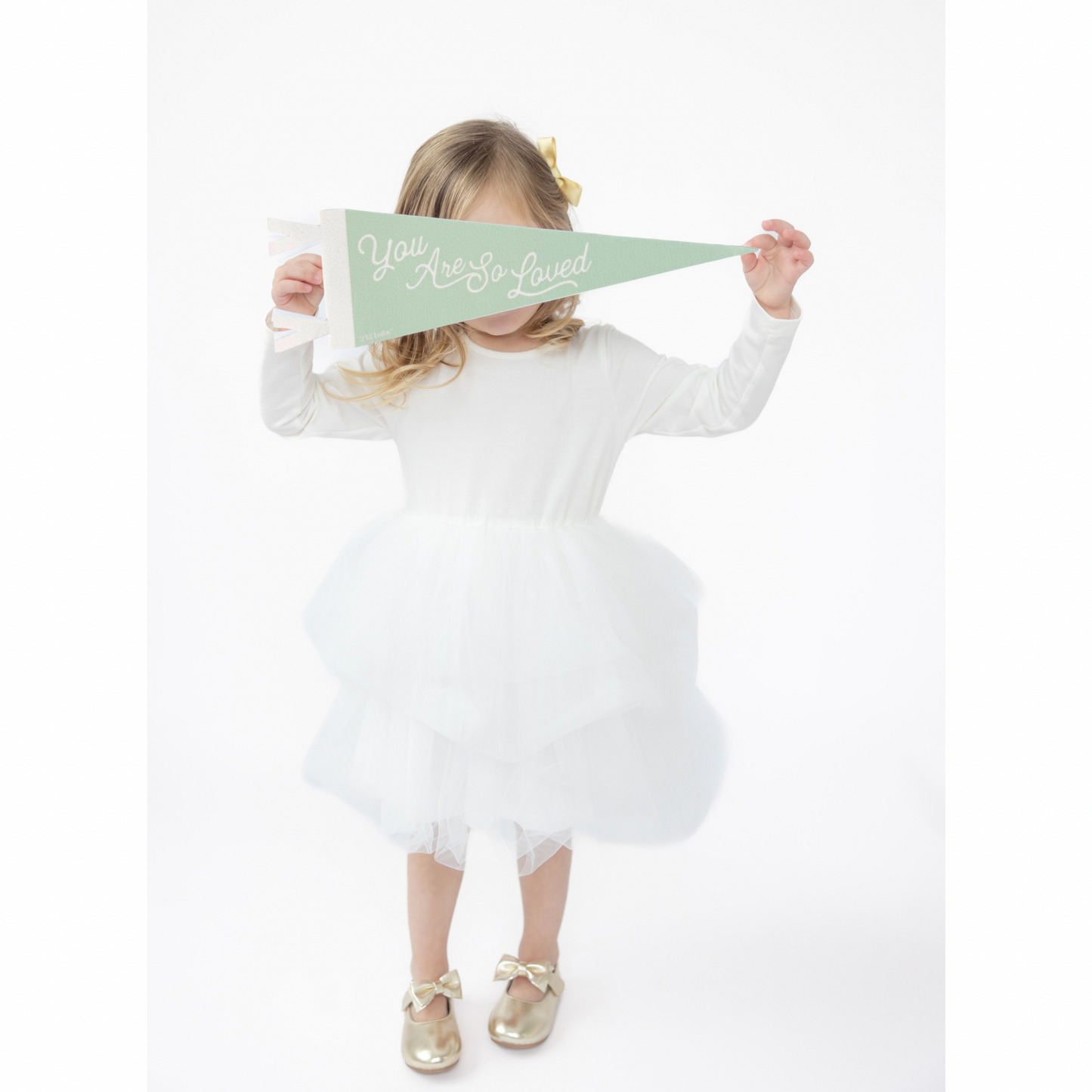 Child in a white dress holding a green nursery decor banner with text on a white background