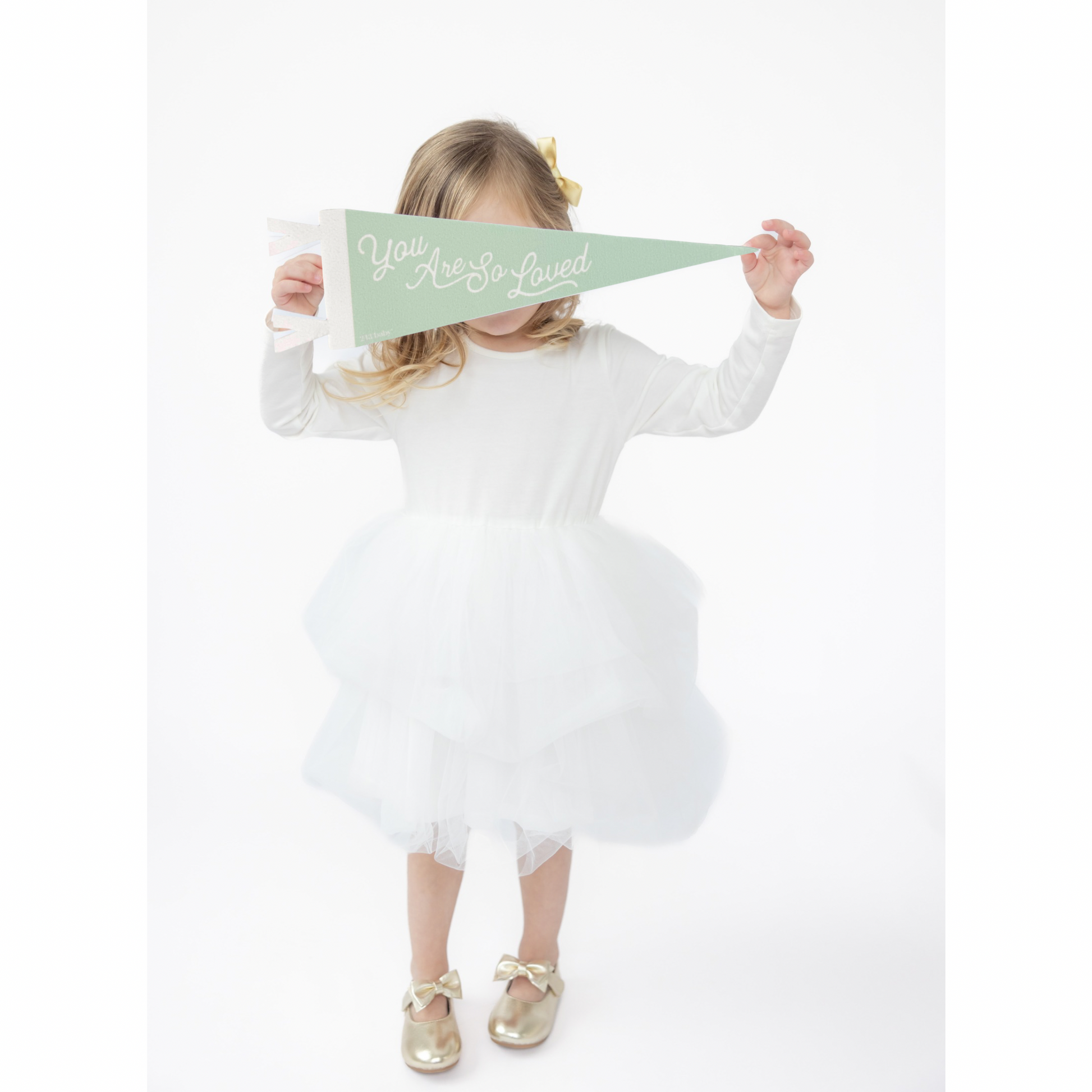 Child in a white dress holding a green nursery decor banner with text on a white background