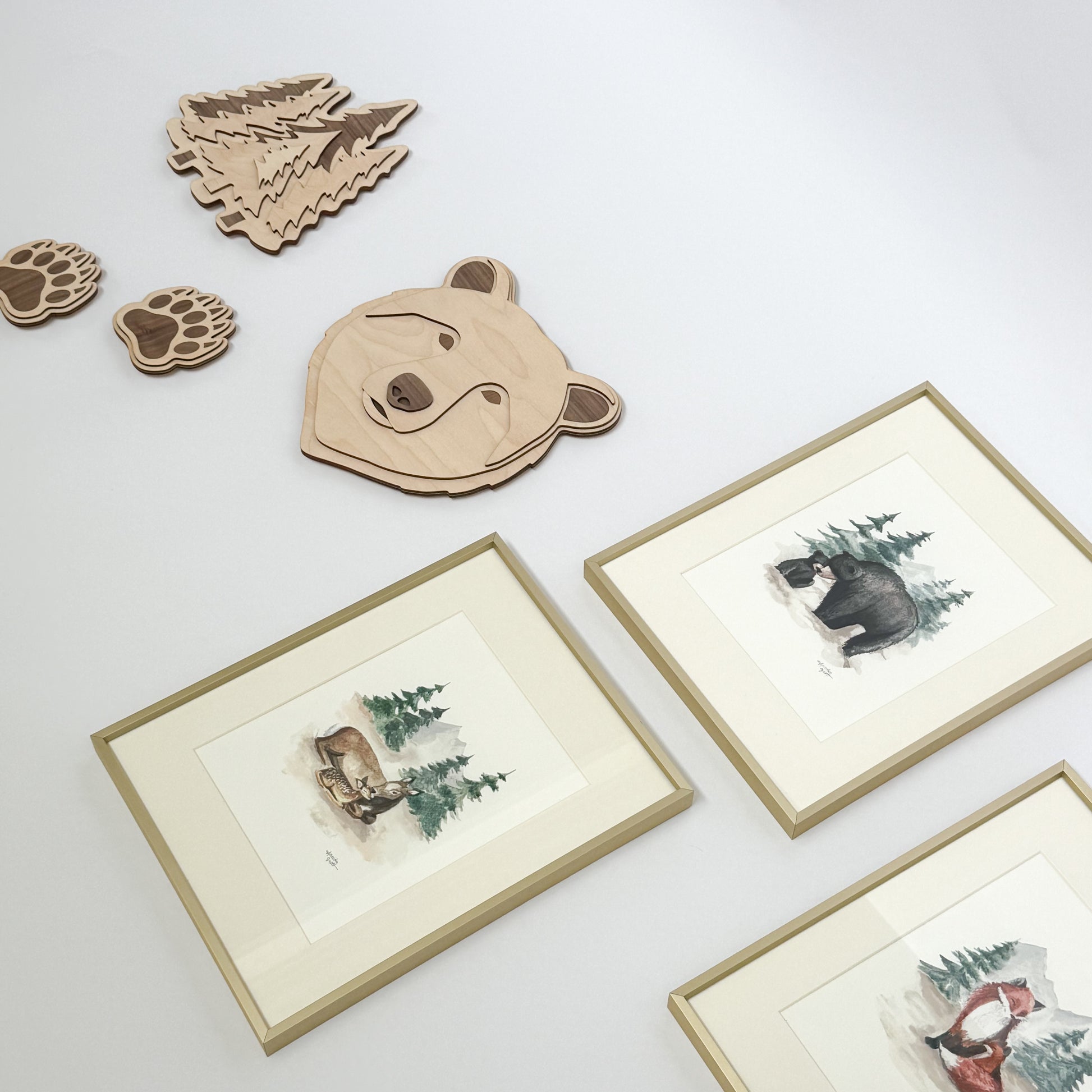 Wooden bear, evergreen trees, and bear paw prints and framed illustrations of woodland creatures in gold frames on a light background