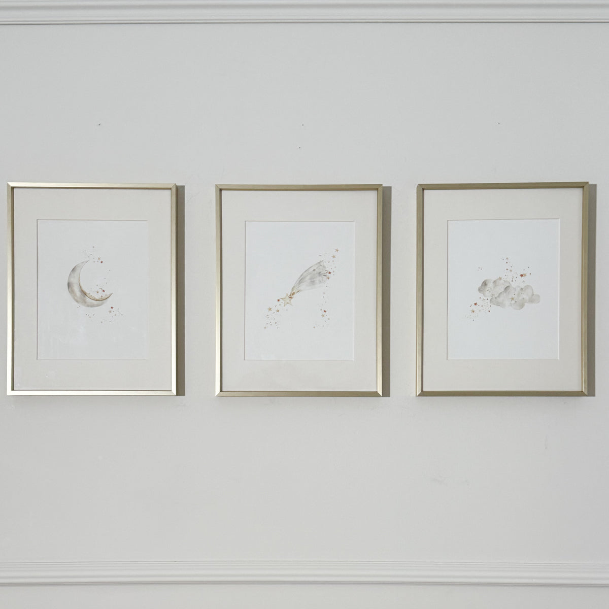 Three framed celestial watercolor art prints with gold frames hanging side-by-side on a white wall with decorative molding.