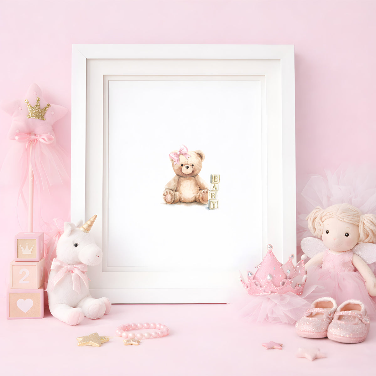 Framed watercolor art print of a cute teddy bear with a pink bow next to baby wooden blocks, styled in a pink nursery setting with plush toys.