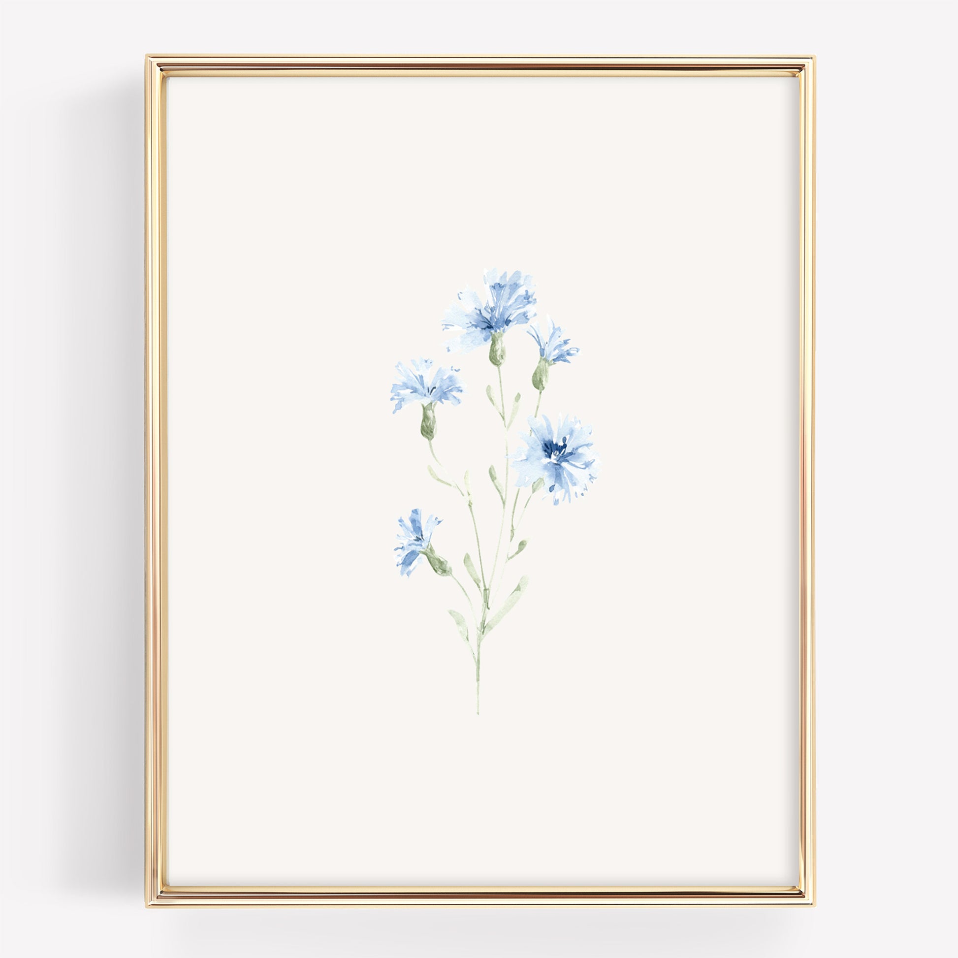 A vertical framed art print featuring a delicate watercolor illustration of blue cornflowers on an off-white background, enclosed in a thin gold frame.