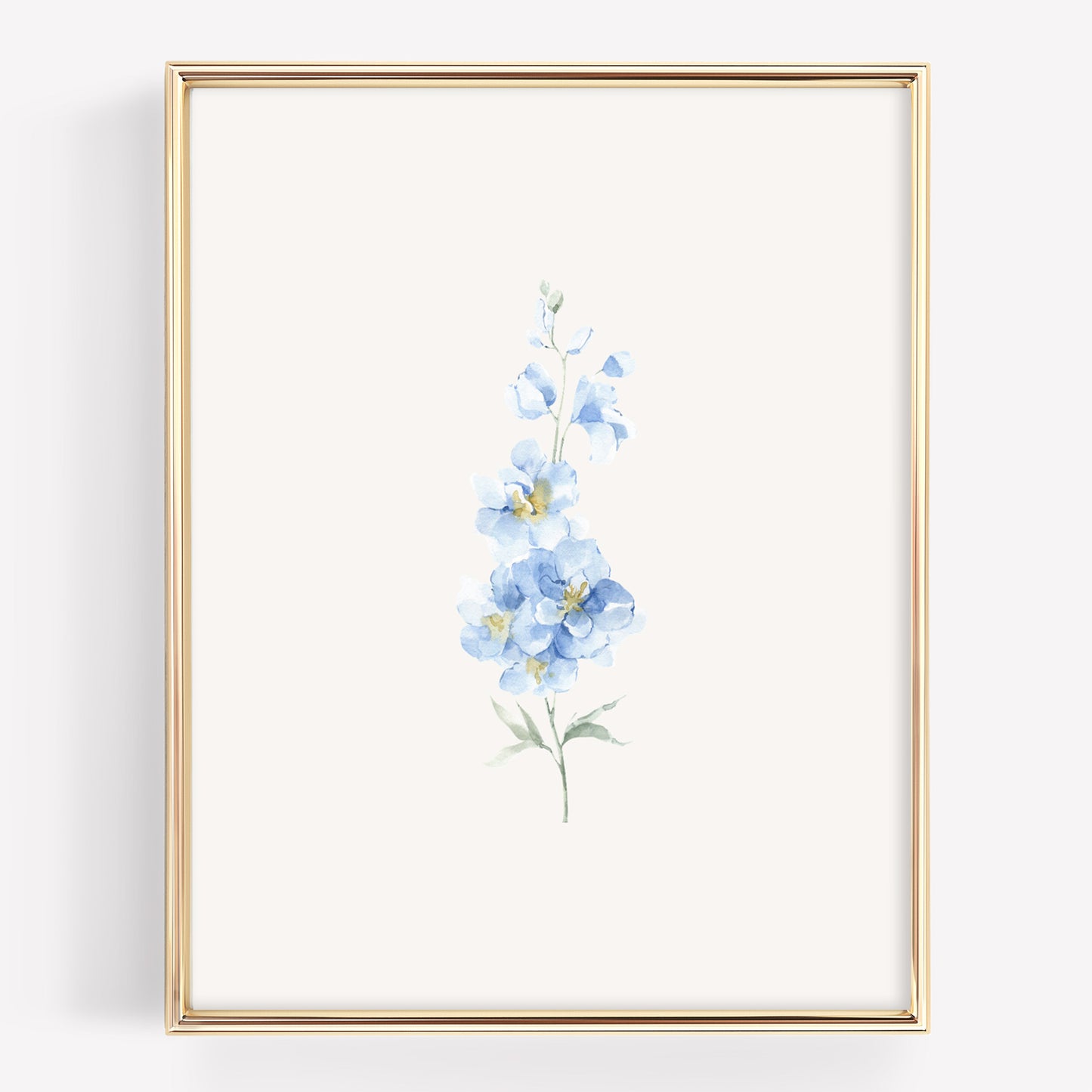 A vertical framed art print featuring a delicate watercolor illustration of light blue flowers with green stems on an off-white background, enclosed in a thin gold frame.