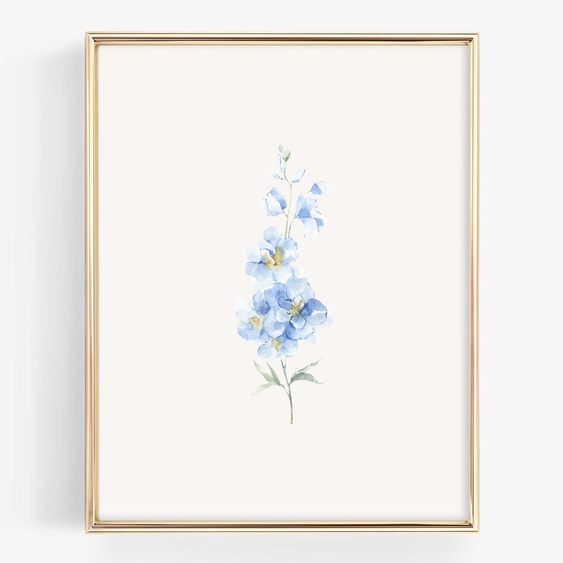 A vertical framed art print featuring a delicate watercolor illustration of light blue flowers with green stems on an off-white background, enclosed in a thin gold frame.