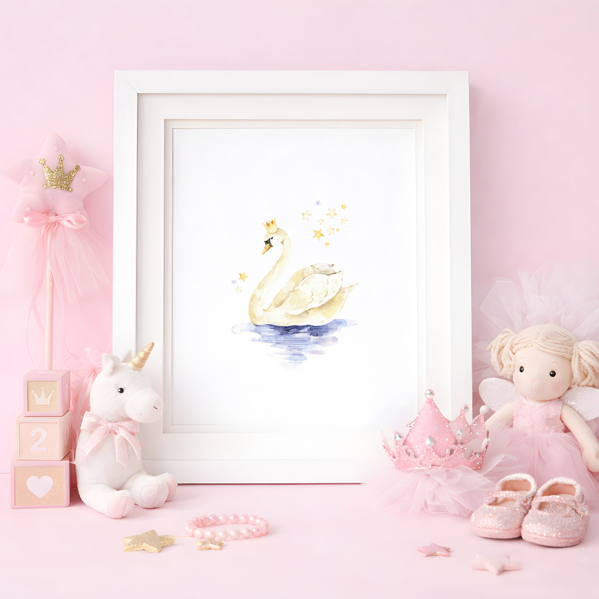 Framed watercolor art print of a graceful swan wearing a tiny gold crown, styled on a pink tabletop with a plush unicorn and princess accessories.