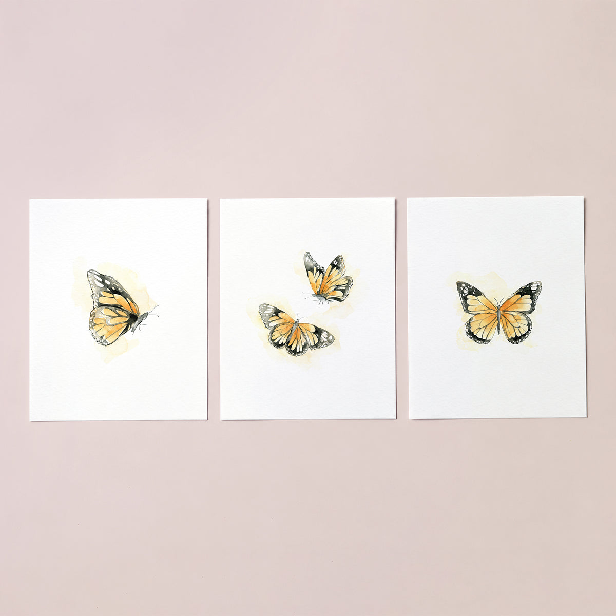 Unframed set of 3 watercolor monarch butterfly art prints on white textured paper displayed on a neutral background.