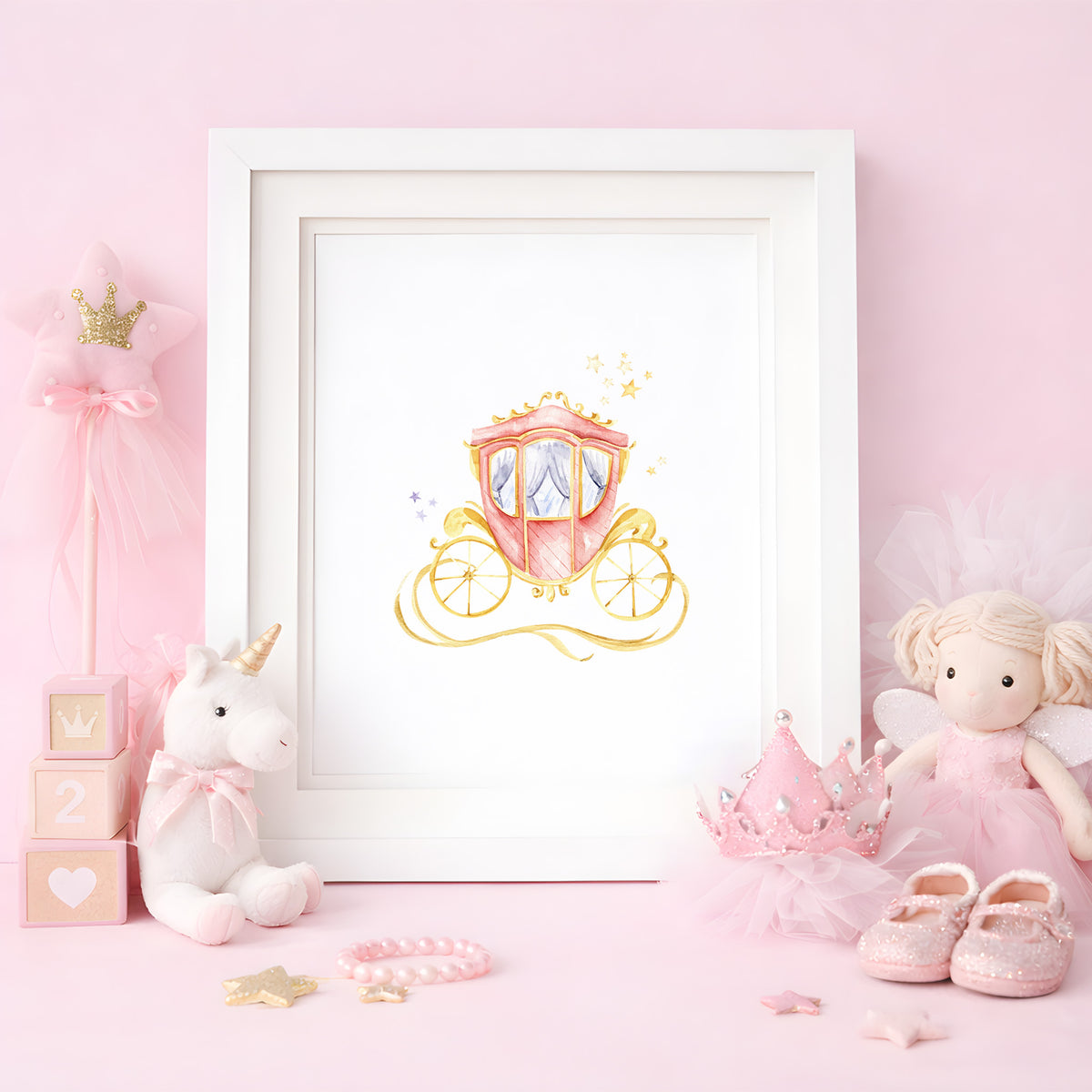 Framed watercolor art print of a pink and gold princess carriage set on a pink desk alongside a plush unicorn, fairy doll, and baby shoes.