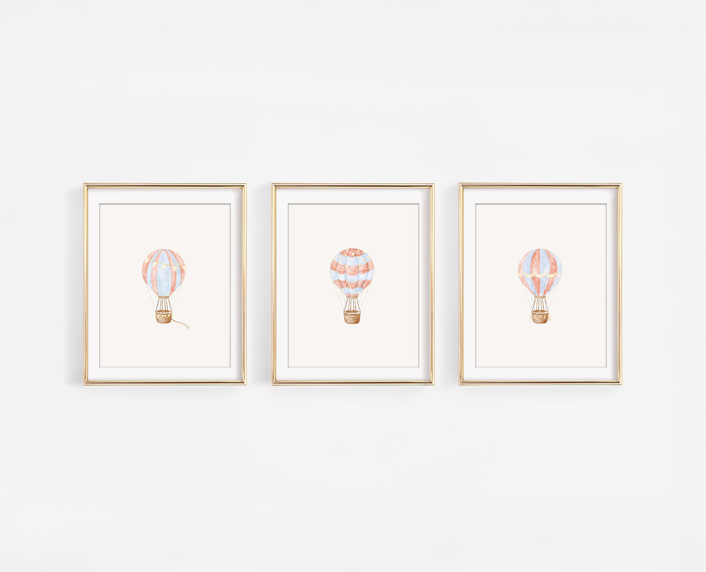 Set of three framed watercolor nursery art prints featuring red, blue, and gold hot air balloons on a clean white wall, 8x10 adventure themed baby room decor.
