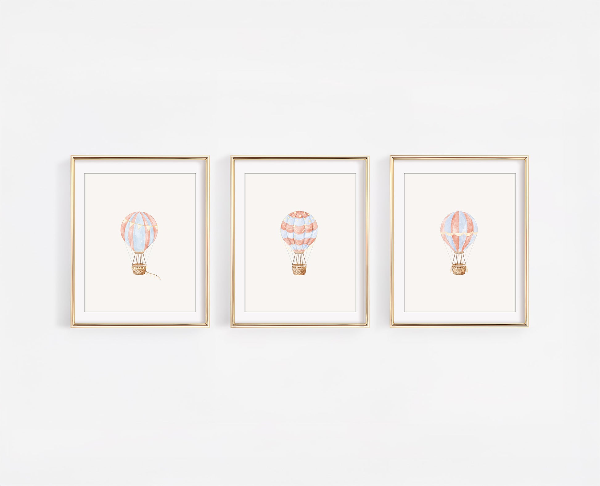 Set of three framed watercolor nursery art prints featuring red, blue, and gold hot air balloons on a clean white wall, 8x10 adventure themed baby room decor.