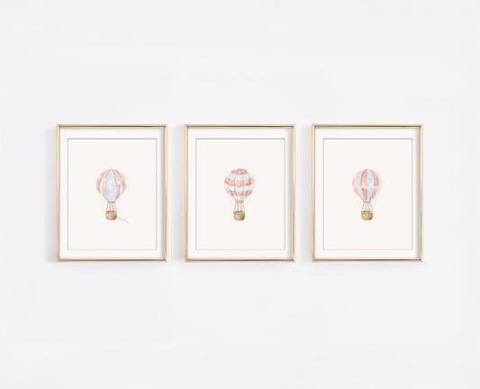 Set of three framed watercolor nursery art prints featuring red, blue, and gold hot air balloons on a clean white wall, 8x10 adventure themed baby room decor.