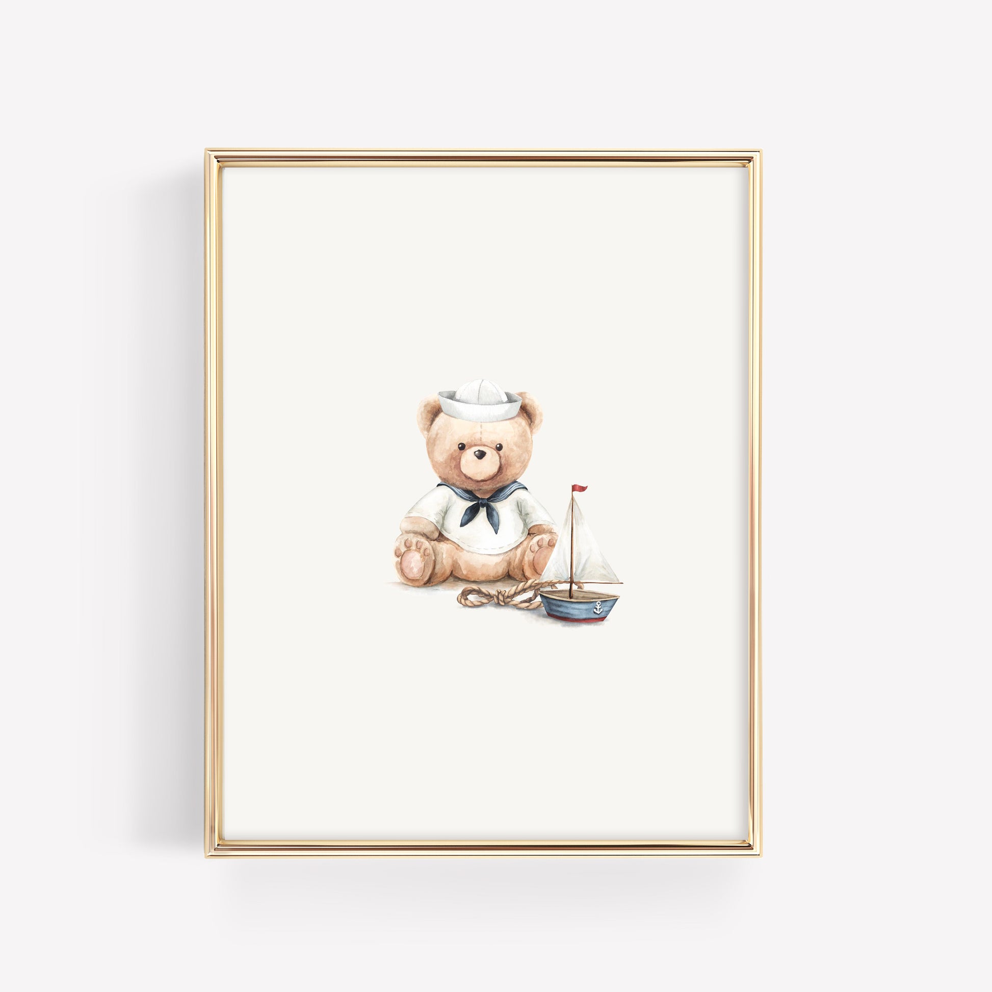 A framed art print featuring a watercolor illustration of a teddy bear in a sailor outfit next to a small sailboat, set in a thin gold frame against a light gray background.