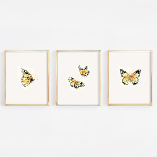 Set of three 8x10 gold-framed nursery prints featuring watercolor monarch butterflies with a soft orange glow, perfect for a gender-neutral or nature-themed baby room.