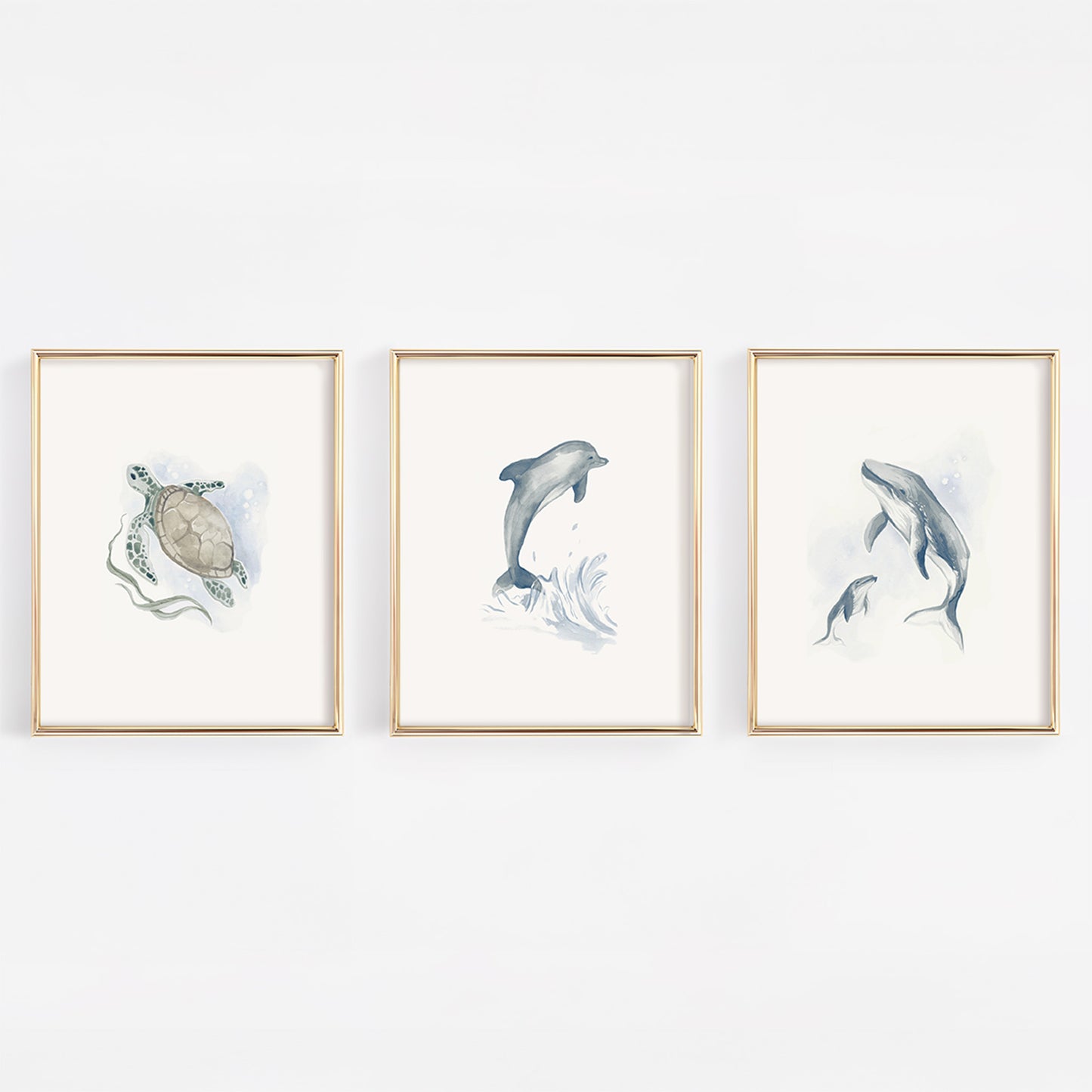 Set of three gold-framed nursery prints featuring watercolor marine life: a gentle sea turtle, a mother and baby humpback whale, and a playful blue dolphin on a clean white background.