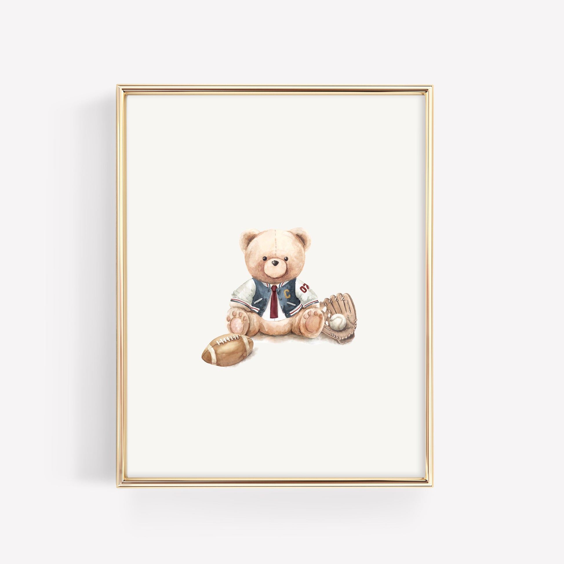 A framed art print featuring a watercolor illustration of a teddy bear dressed in a varsity jacket, sitting with a baseball and football, enclosed in a thin gold frame against a light gray background.