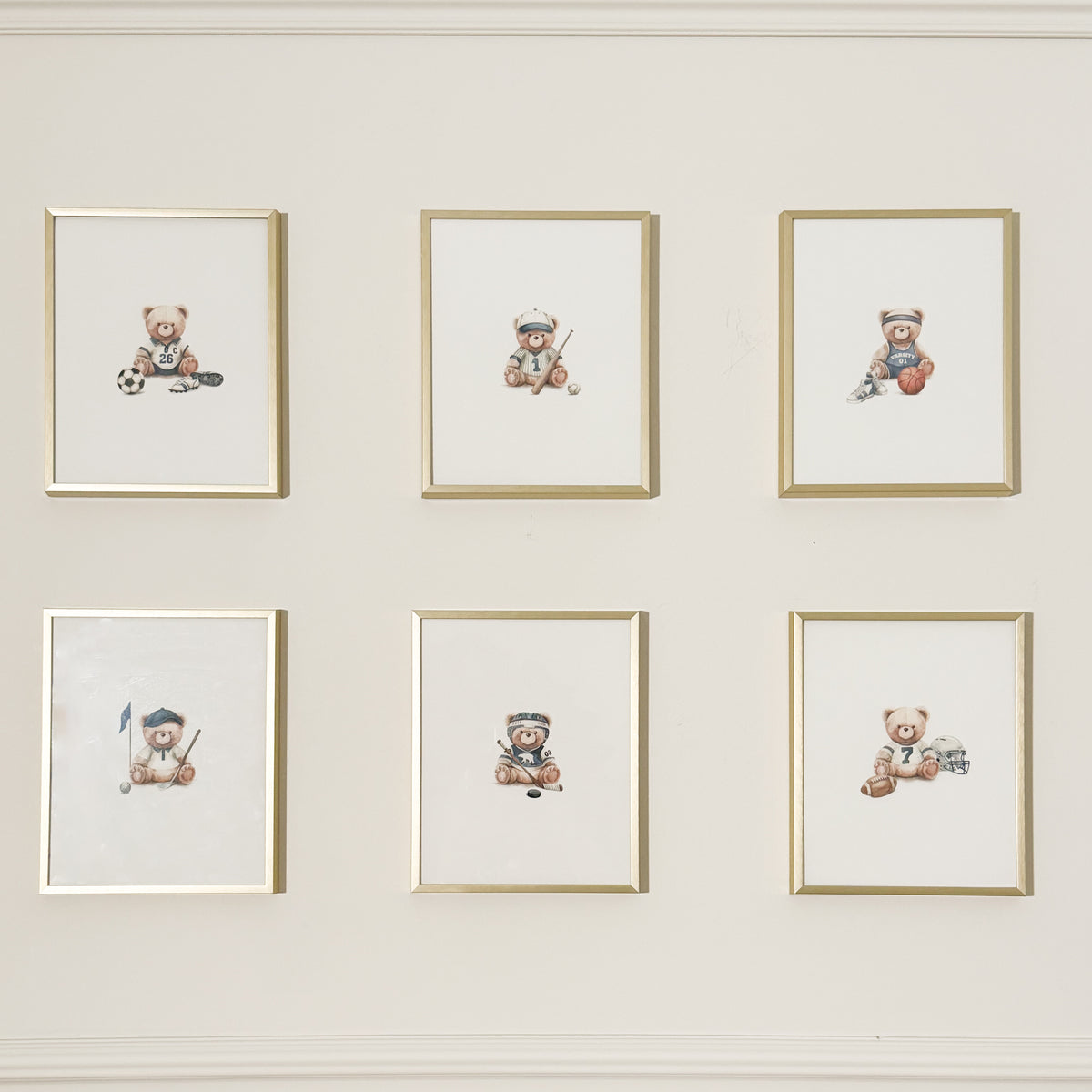 Six framed watercolor prints of teddy bears playing sports, arranged in a 2x3 grid on a cream-colored wall.