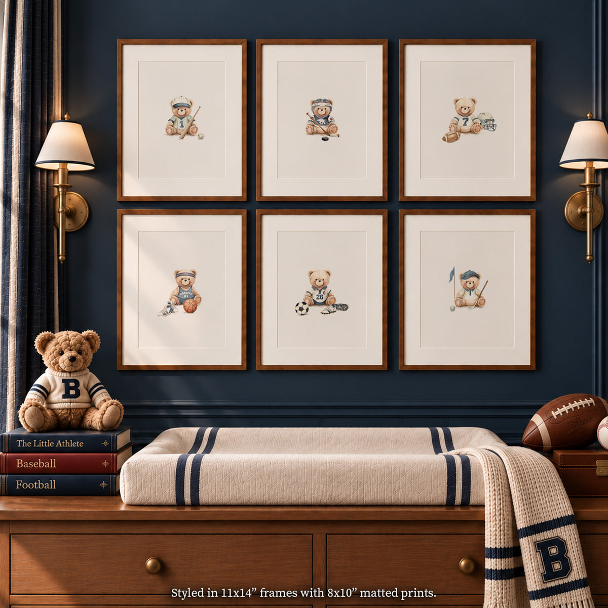 Close-up nursery view of 6 watercolor vintage sports bear art prints in 11x14 matted wood frames above an oak changing table, styled with a striped changing pad, letter blanket, books, teddy bear, and sports balls on a dark navy wall.