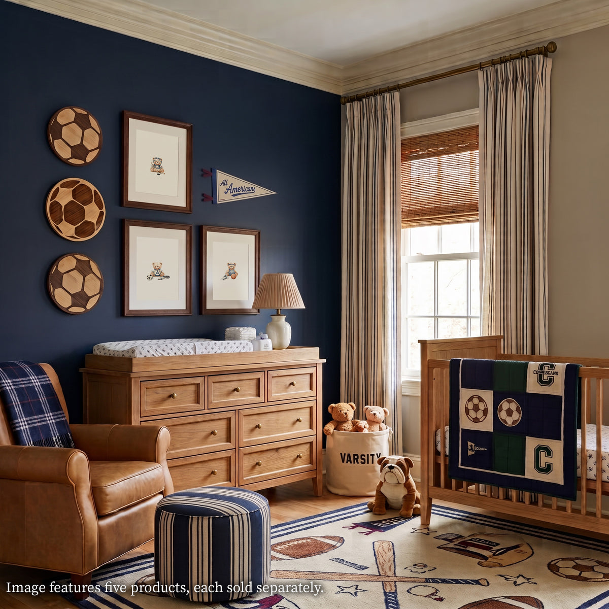 Vintage sports-themed nursery featuring a navy accent wall with three round wooden soccer balls, a set of framed teddy bear prints, and a felt pennant, styled above a light oak changing dresser