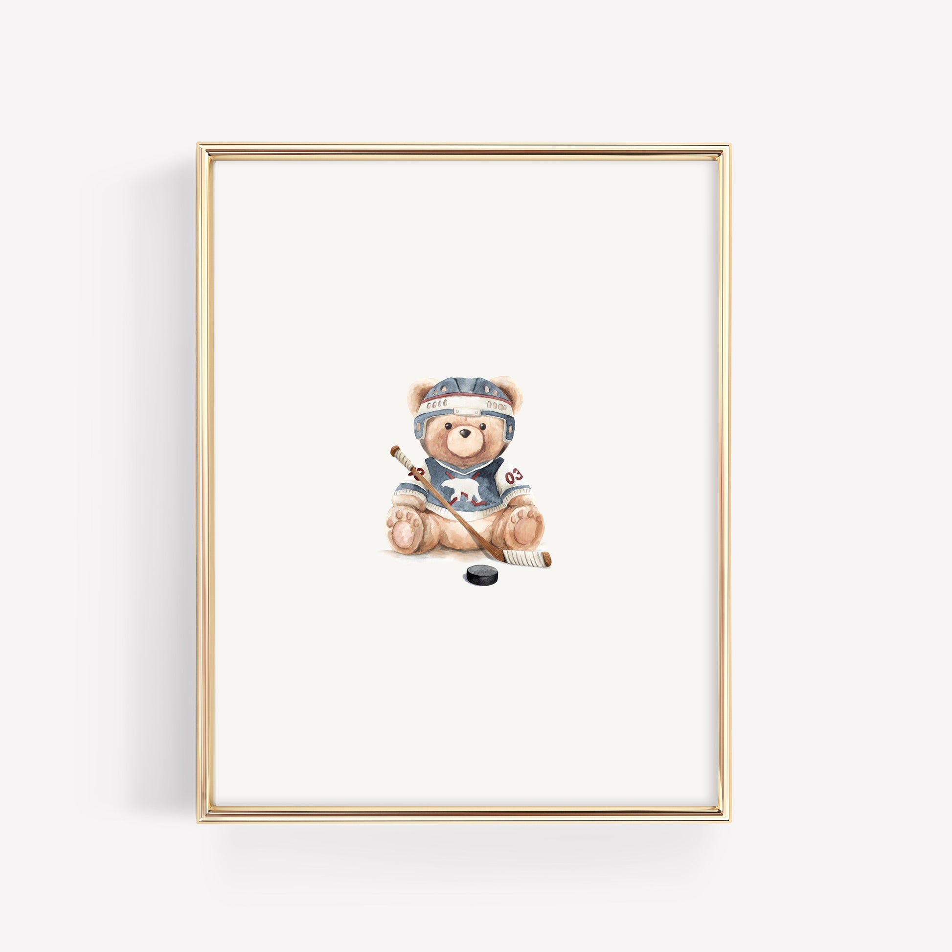 A framed art print featuring a watercolor illustration of a teddy bear wearing a hockey helmet and jersey, sitting with a hockey stick and puck, set in a thin gold frame against a white background.