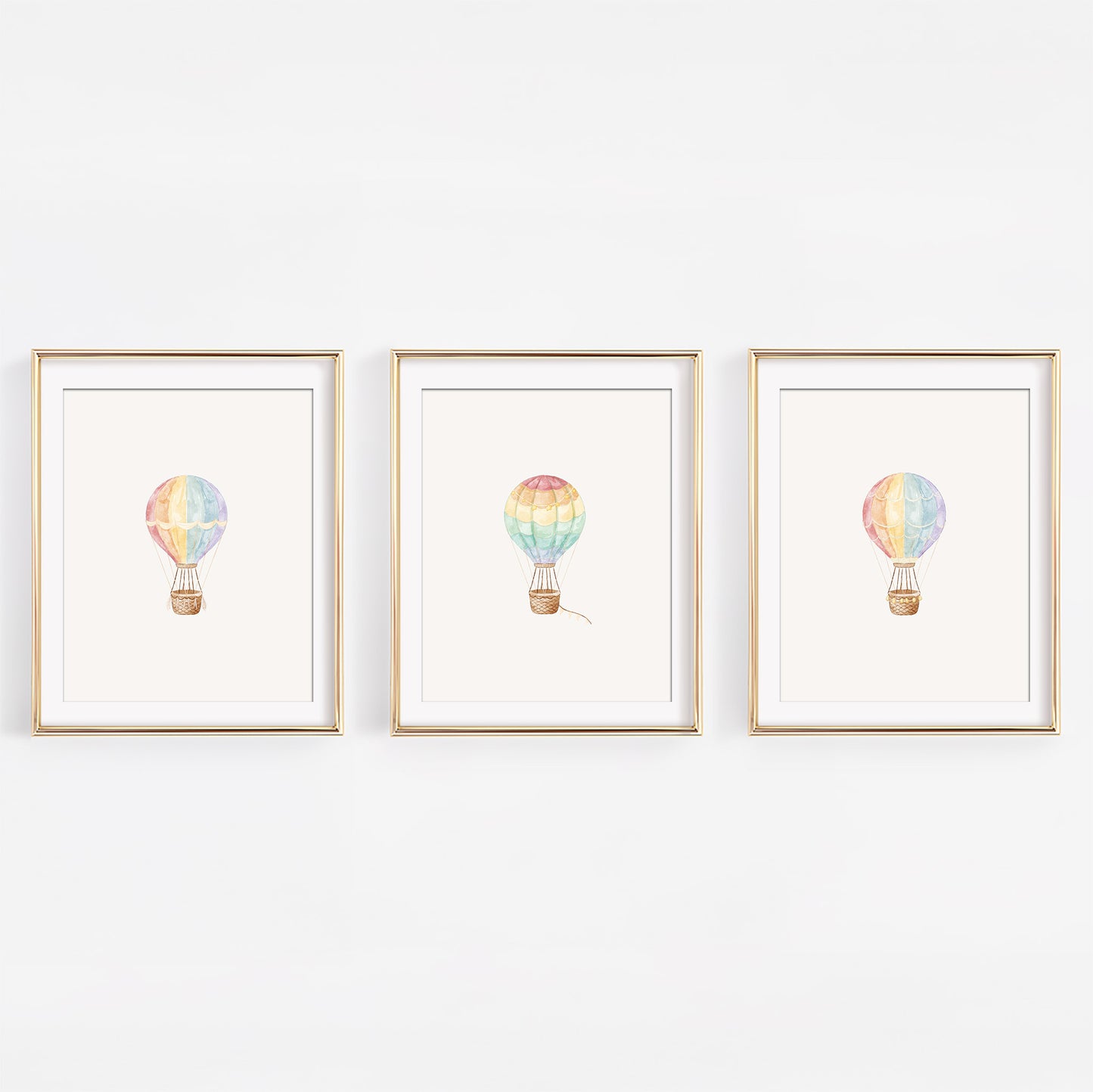 Set of three watercolor rainbow hot air balloon nursery art prints displayed in frames on a white wall.
