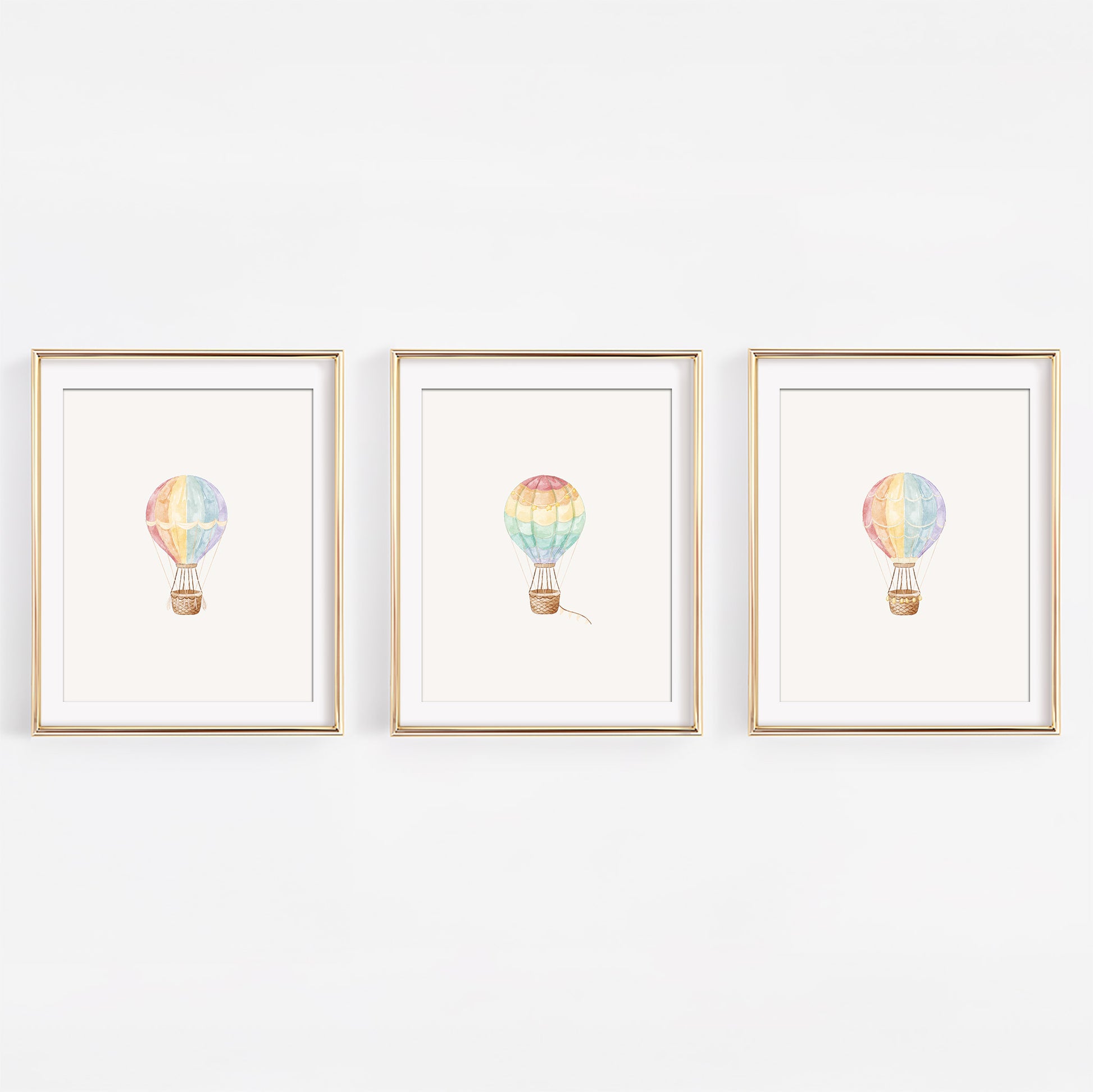 Set of three watercolor rainbow hot air balloon nursery art prints displayed in frames on a white wall.