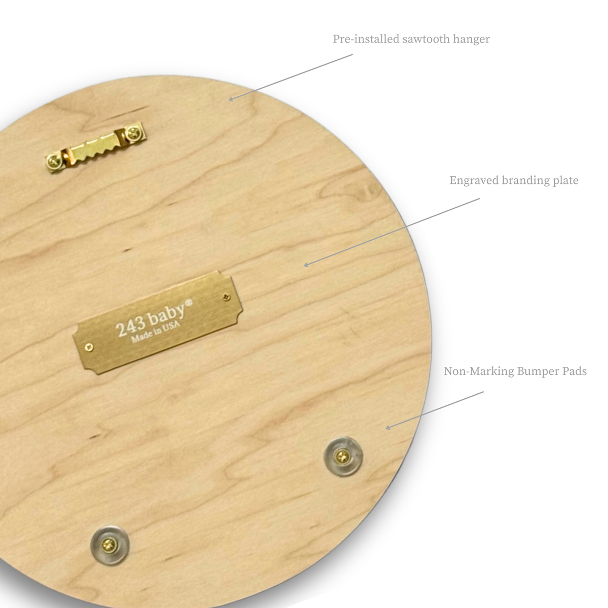 Close-up view of the back of a round wooden basketball wall decor, showing the pre-installed gold sawtooth hanger, an engraved brass '243 baby® Made in USA' branding plate, and clear non-marking bumpers on natural maple wood.