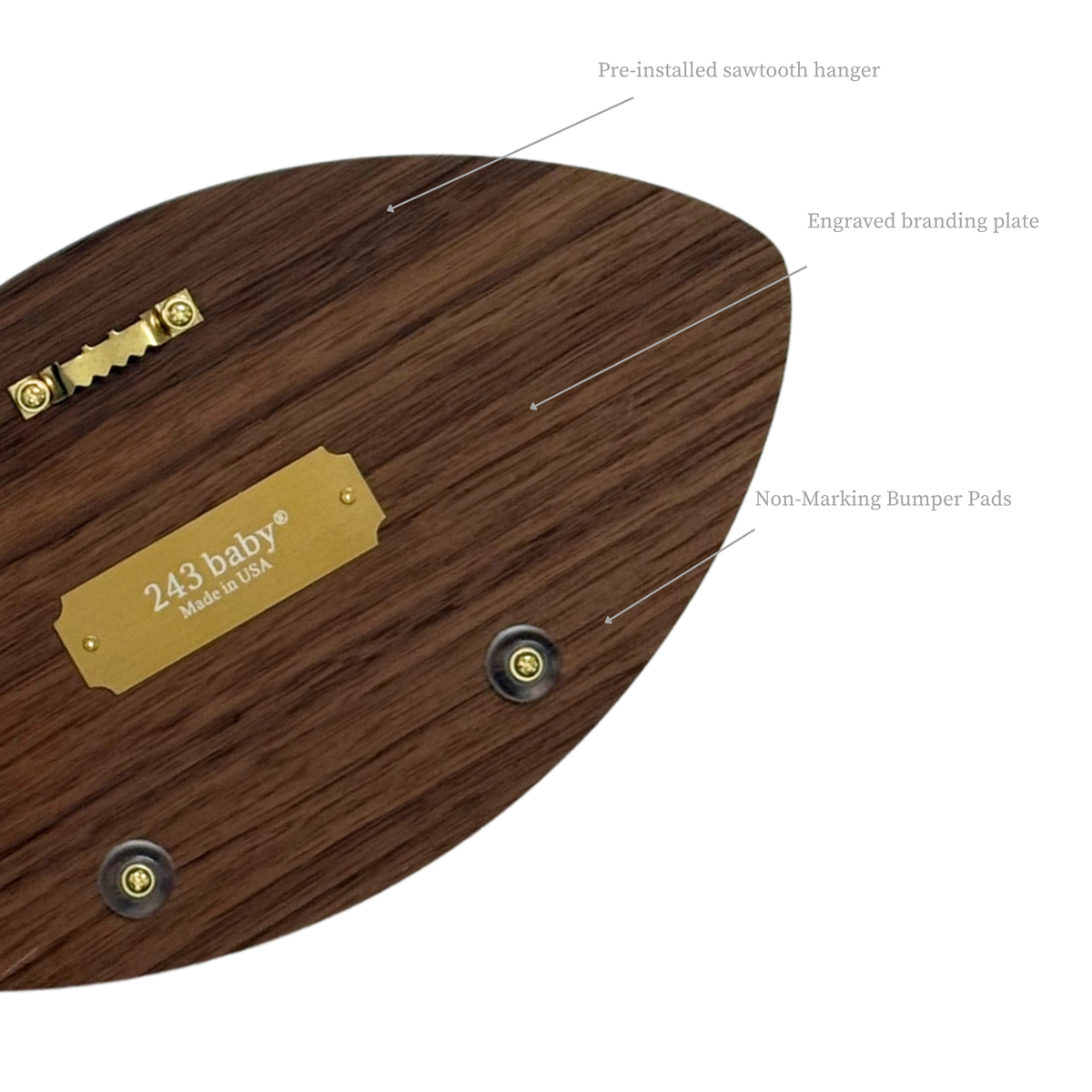 Close-up view of the back of a wooden football wall decor, displaying the pre-installed sawtooth hanger, translucent non-marking bumpers, and the '243 baby® Made in USA' engraved brass plate on natural wood.